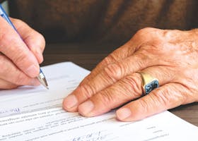 Practice Area Close-up of a senior adult signing a legal document with a focus on hand and gold ring.